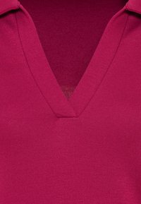 Fuksia-kangas, jossa on V-pääntie, esitellen sileää pintaa ja hienovaraista kiiltoa. Keskittyminen vaatteen yksityiskohtiin ilman häiriötekijöitä.