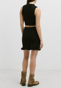Zwart textuur crop top en mini rok set met ruche rand. Model draagt bruine suède enkellaarsjes met een gespsluiting.