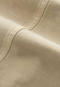 Gros plan sur un tissu beige avec une double surpiqûre visible, montrant la texture et les détails des coutures sur un matériau doux tissé.