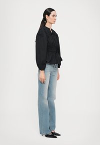 Svart topp med pufferm, med frontknute, kombinert med lyseblå utsvungne jeans og spisse svarte hæler. Glatt tekstur, avslappet passform.