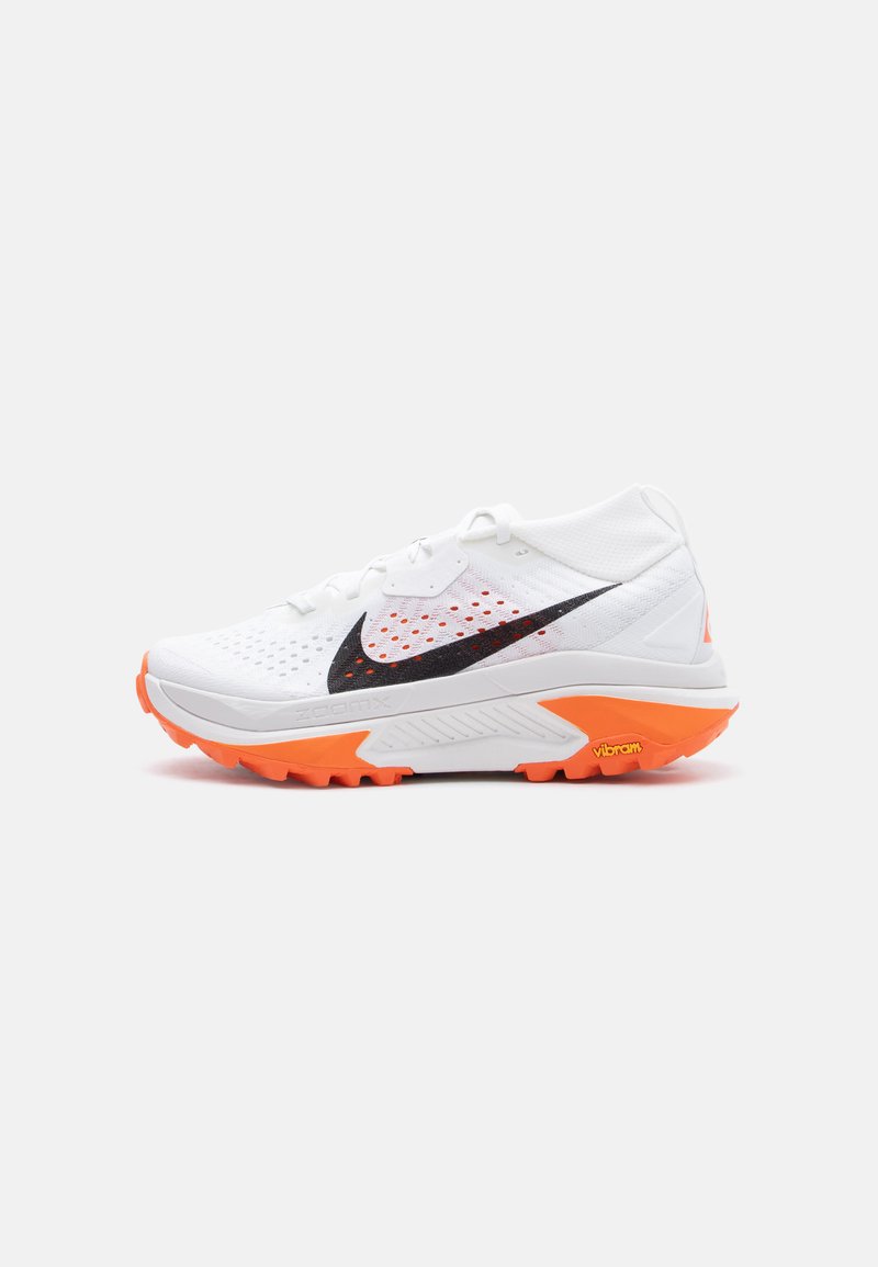 Λευκό αθλητικό παπούτσι με μαύρο λογότυπο Nike, διαπνεόμενο επάνω μέρος και φωτεινή πορτοκαλί σόλα Vibram, σχεδιασμένο για τρέξιμο σε εξωτερικούς χώρους.