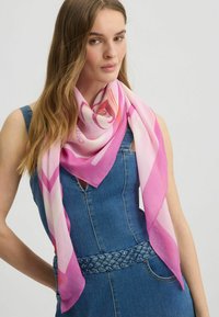 Écharpe en soie rose avec des motifs géométriques, drapée autour du cou. Texture douce et dégradé de nuances allant du rose clair au rose foncé.