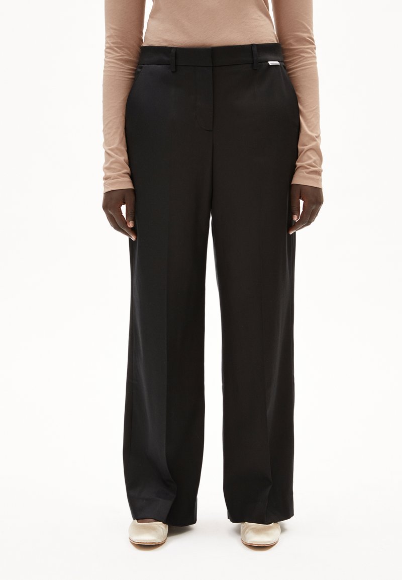 Zwarte wijde broek met een gladde textuur, met een rechte voorkant, riemlussen en een klein zilveren logo detail nabij de tailleband.