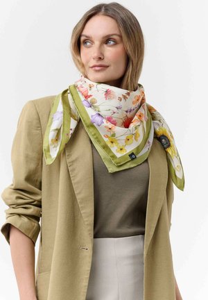 Woman wearing beige blazer, olive green top, and a floral silk scarf with yellow, purple, and orange flowers tied around her neck.