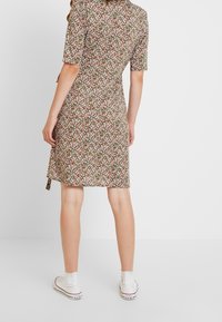 Kwiatowa sukienka w kolorze brązowym z krótkimi rękawami, zdobiona małym, wielokolorowym wzorem kwiatowym. Noszona z białymi trampkami za kostkę.