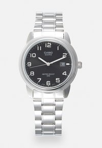 Montre quartz avec un bracelet en acier inoxydable argenté, cadran noir rond, index horaires blancs et un affichage de date à 3 heures. Étanche jusqu'à 50 mètres.