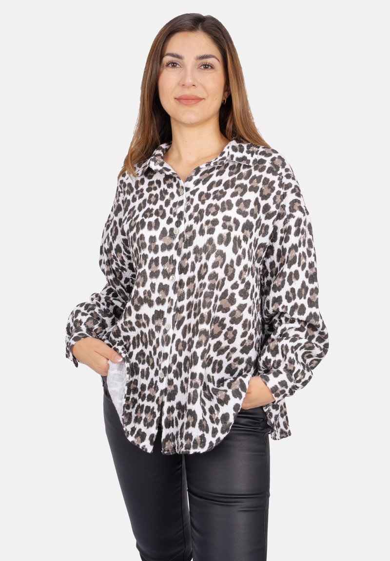 Leopardmuster-Hemd mit Knopfverschluss aus leichtem Stoff, mit Kragen, langen Ärmeln und Fronttaschen, kombiniert mit schwarzen, enganliegenden Hosen.
