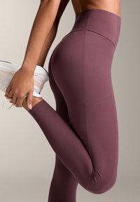 Vysoké elastické legíny v tmavej fialovej farbe, vyrobené z hladkej elastickej tkaniny. Majú priliehavý strih s plochými švami a jednoduchým pásom.