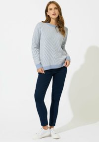 Jasnoniebieski sweter w wzór zygzaka, w połączeniu z ciemnymi dżinsami i białymi sneakersami. Sweter ma prążkowany dekolt i mankiety.