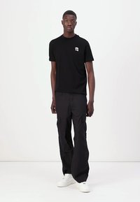 Tricou din bumbac negru cu un logo alb pe partea stângă a pieptului, asortat cu pantaloni cargo negri, cu multiple buzunare și o croială largă.
