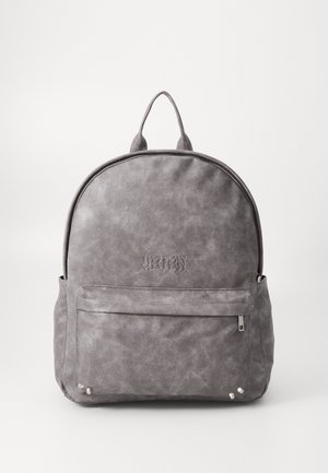 Pelēka mākslīgās ādas mugursoma ar apaļu formu, embossētu logotipu, priekšējo rāvējslēdzēja kabatu un sudraba aparatūras akcentiem. Gluda, teksturēta virsma.