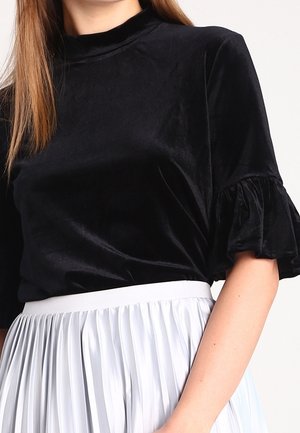 Zwarte fluwelen top met korte mouwen en ruches aan de mouwen, gecombineerd met een witte geplooide hoge taille rok.