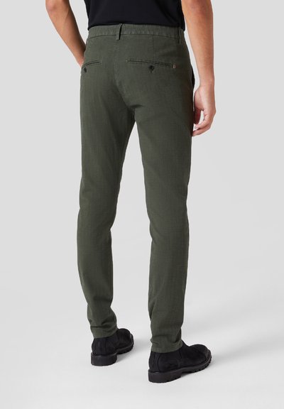 Pantaloni verdi slim-fit realizzati in tessuto testurizzato, con due tasche posteriori con bottoni e un design a gamba dritta. Scarpe nere visibili.