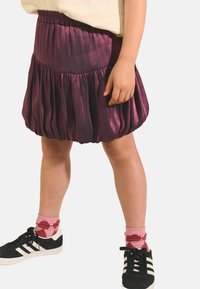Jupe bulle en satin violet avec taille élastique, présentant un design volumineux. Baskets noires et blanches avec des chaussettes à motifs roses.