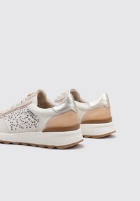 Zapatillas para mujer en cuero crema con patrones triangulares recortados, detalles metálicos en plata y una suela blanca texturizada.