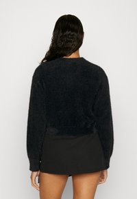 Pull noir en peluche à manches longues, col rond et coupe courte, associé à une jupe noire unie. Tissu doux et texturé.