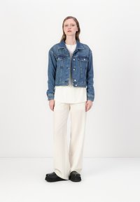 Keskmise sinise tooniga denim-jakk, lühendatud disainiga, kahe rinnataskuga; paaritatud valge särgi ja kreemjate laiadest pükstega. Mustad platvormkingad.