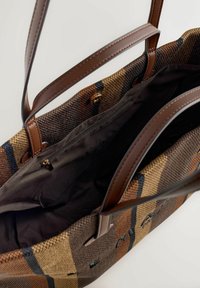 Nákupná taška s hnedými koženými rukoväťami a tkaným vonkajším povrchom v hnedých a béžových kockovaných vzoroch. Má tmavé látkové vnútro so zipsovou vreckom.