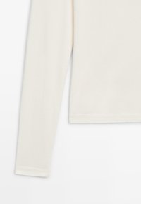 Langærmet, cremefarvet top lavet af blødt stof. Har et enkelt design med en lige kant og pæne sømme langs kanterne.