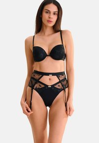 Ensemble de lingerie noire comprenant un soutien-gorge rembourré et un body en maille transparente avec broderies florales, bretelles réglables et accents de porte-jarretelles.