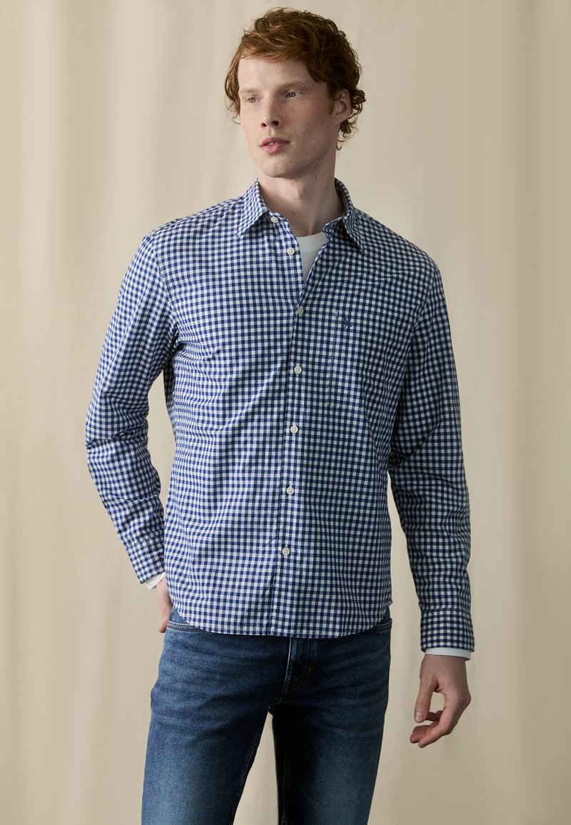 Blå og hvit rutete skjorte med lange ermer og knapp-ned krage, sammen med blåjeans. Stoffet ser glatt og lett ut.