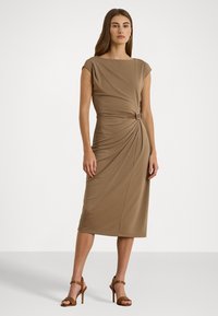 Brun, knelangsdress med korte ermer, rynket sidet detalj og belteaksent. Glatt, elastisk stoff. Båret med brune stroppede hæler.