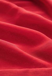Tela roja con una textura suave, que presenta pliegues suaves y una superficie ligeramente brillante, destacando su rico color y profundidad.