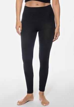 Vrouw draagt zwart geribbelde, hooggerichte leggings en staat blootsvoets tegen een effen witte achtergrond.