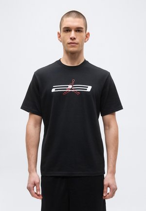 Mladý muž s krátkymi vlasmi v čiernom tričku s bielym a červeným abstraktným športovým logom na jednoduchom svetlom pozadí.