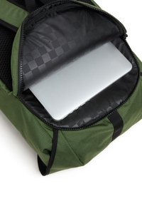 Sac à dos vert avec fermeture éclair noire partiellement ouverte, montrant un ordinateur portable argenté à l'intérieur d’un compartiment rembourré avec une doublure noire à carreaux.