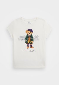 Weißes Baumwoll-T-Shirt mit einer bunten Bärenillustration, die einen grünen Mantel, eine lila Baskenmütze und braune Schuhe trägt, mit Branding darunter.