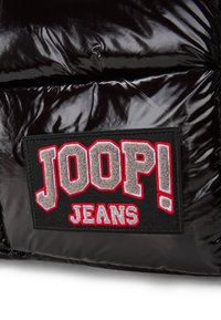Zwart glanzend pufferstof met prominente, gestructureerde label met "JOOP!" in grijs en rood, naast "JEANS." Het ontwerp is gewatteerd en volumineus.