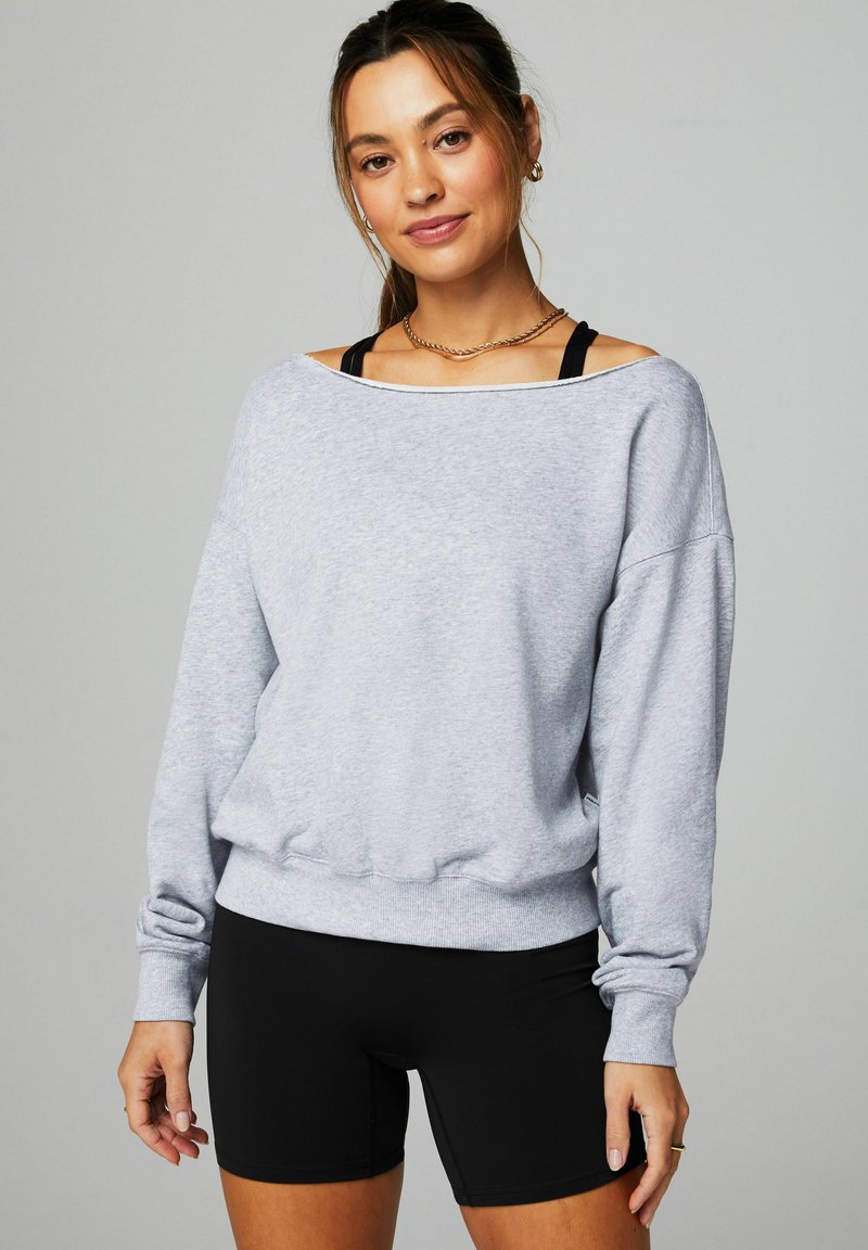 Sweatshirt gris à encolure large et manches longues, associé à un short de vélo noir. Texture douce, coupe décontractée, avec des poignets côtelés.