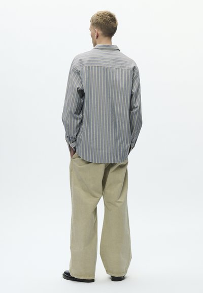 Črtasta srajca modro-bele barve z dolgimi rokavi, kombinirana z bež hlačami širokih nog. Gladek material z udobnim krojem in gumbnimi detajli.
