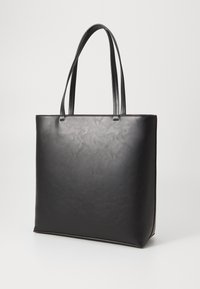 Sac fourre-tout en faux cuir noir avec deux longues anses. Texture lisse, forme rectangulaire, design minimaliste et sans quincaillerie visible.