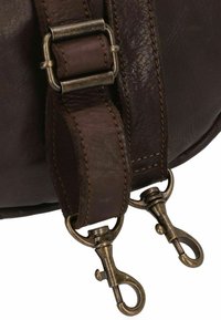 Tracolla in pelle marrone scuro con due ganci a moschettone in ottone anticato e bordi cuciti, attaccata a un angolo di una borsa in pelle.