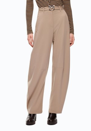 Pantaloni beige a gamba larga con dettagli sulla cucitura frontale, abbinati a stivali neri robusti e a una maglia a righe marrone e nera a maniche lunghe infilata dentro.