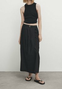 Haut en tricot noir raccourci associé à une longue jupe plissée noire et des tongs noires. Design simple avec une coupe décontractée et des accents minimaux.