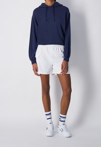 Námořnická zkrácená mikina s dlouhými rukávy, bílé šortky s elastickým pasem, pruhované bílé ponožky a bílé tenisky s černými akcenty.