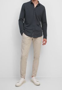 Slim-Fit-Hemd mit langen Ärmeln aus dunkelgrauer Baumwolle, mit button-down Kragen, kombiniert mit beigen Chinos und weißen Turnschuhen.