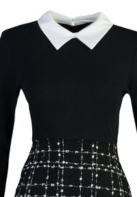 Robe noire à manches longues avec col pointu blanc et partie jupe à carreaux texturée noir et blanc à la taille.
