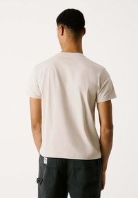 Lys beige kortærmet t-shirt med rund halsudskæring, glat bomuldsstruktur og lige kant, parret med mørkegrå cargo-bukser med synlige lommer.
