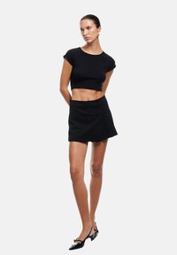 Musta lyhyt cropped t-paita yhdistettynä mustaan mini-hameeseen, jossa on nauha-akkentteja, sileä kangas ja tiukka muotoilu. Patentoitu nahka- tai lakattu ballerina on täydellinen viimeistely asulle.