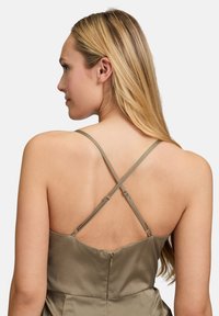 Zielona satynowa sukienka w odcieniu oliwkowym z niskim tyłem, krzyżującymi się ramiączkami oraz zapięciem na zamek. Gładka tekstura połączona z dopasowaną sylwetką.