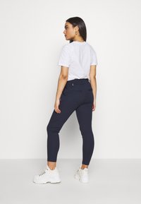 Calças leggings em azul marinho com um design ajustado, faixa elástica na cintura e dois bolsos traseiros, acompanhadas de uma t-shirt branca e ténis brancos de solado grosso.