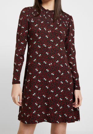 Robe noire à manches longues, présentant un motif floral de fleurs rouges et blanches. Le matériau est doux ; la coupe est évasée avec un col froncé.