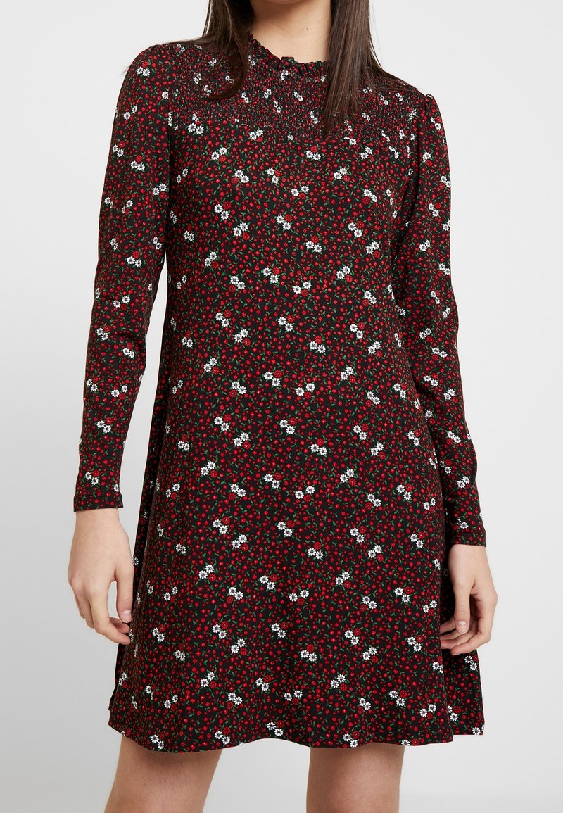 Vestido negro de manga larga, con un patrón floral de flores rojas y blancas. El material es suave; la forma es línea A con un escote fruncido.