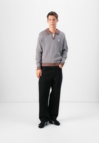 Gray knitted sweater with a brown collar, featuring a v-neck and ribbed hem. Worn with black wide-leg trousers and black sneakers.