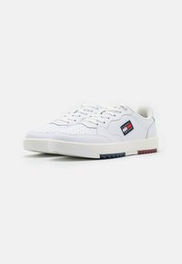 Białe sneakersy z perforowanymi detalami, płaskimi sznurowadłami, wyściełanym kołnierzem i markową metką. Podeszwa z niebieskimi i czerwonymi akcentami. Materiał gumowy.
