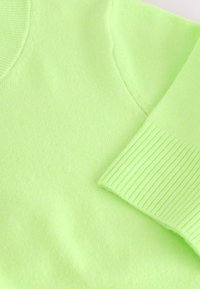 Pull en tricot vert clair avec poignets côtelés et col rond, mettant en valeur la texture douce et les détails des coutures.